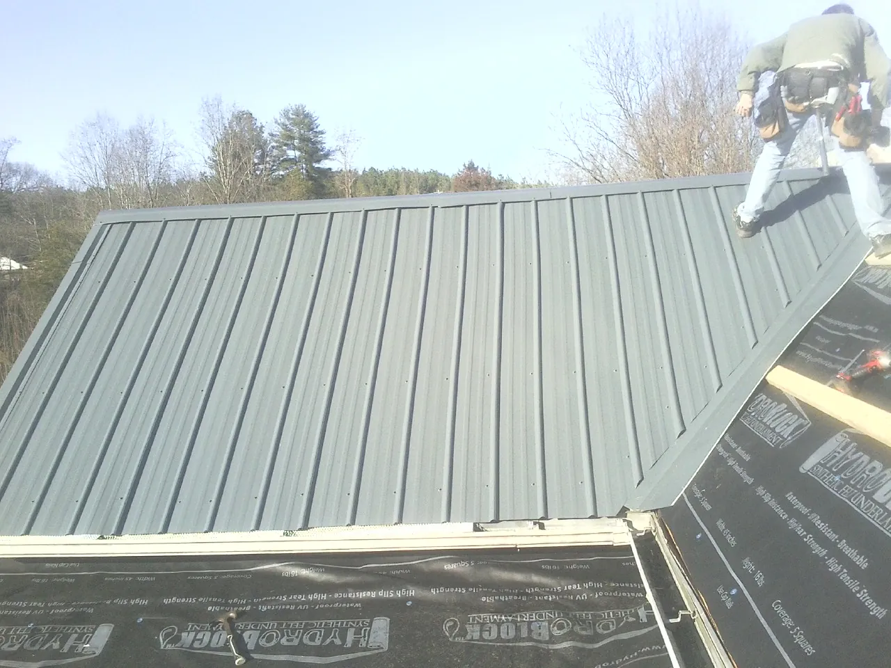 Crew installing dark green standing seam panels over synthetic underlayment in Tobias