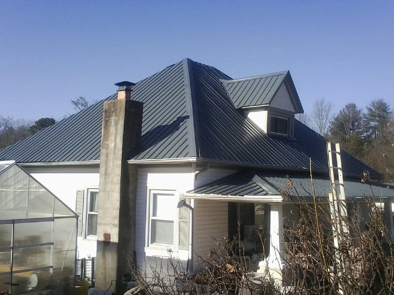 Dark blue standing seam metal roof on a white farmhouse with dormer — Slate & Tile Roof Repair by Roofing Brothers in Tobias