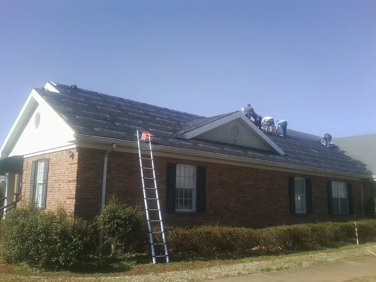 Crew tearing shingles off a brick ranch roof with a ladder set — Emergency Roof Repair work by our crew in Tobias
