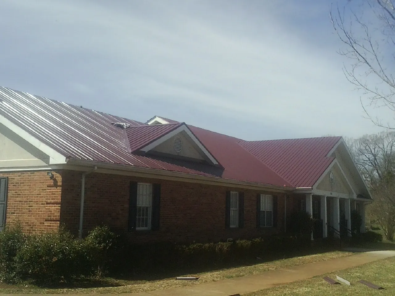 Red metal roof with gabled entries on a long brick building, from a Hail Damage Roof Repair job in Tobias