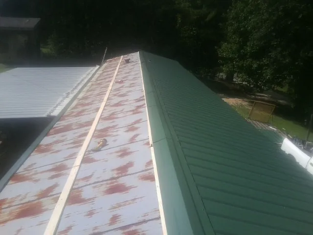 Old rusted panels beside newly installed green metal roofing — Wind Damage Roof Repair by Roofing Brothers in Tobias