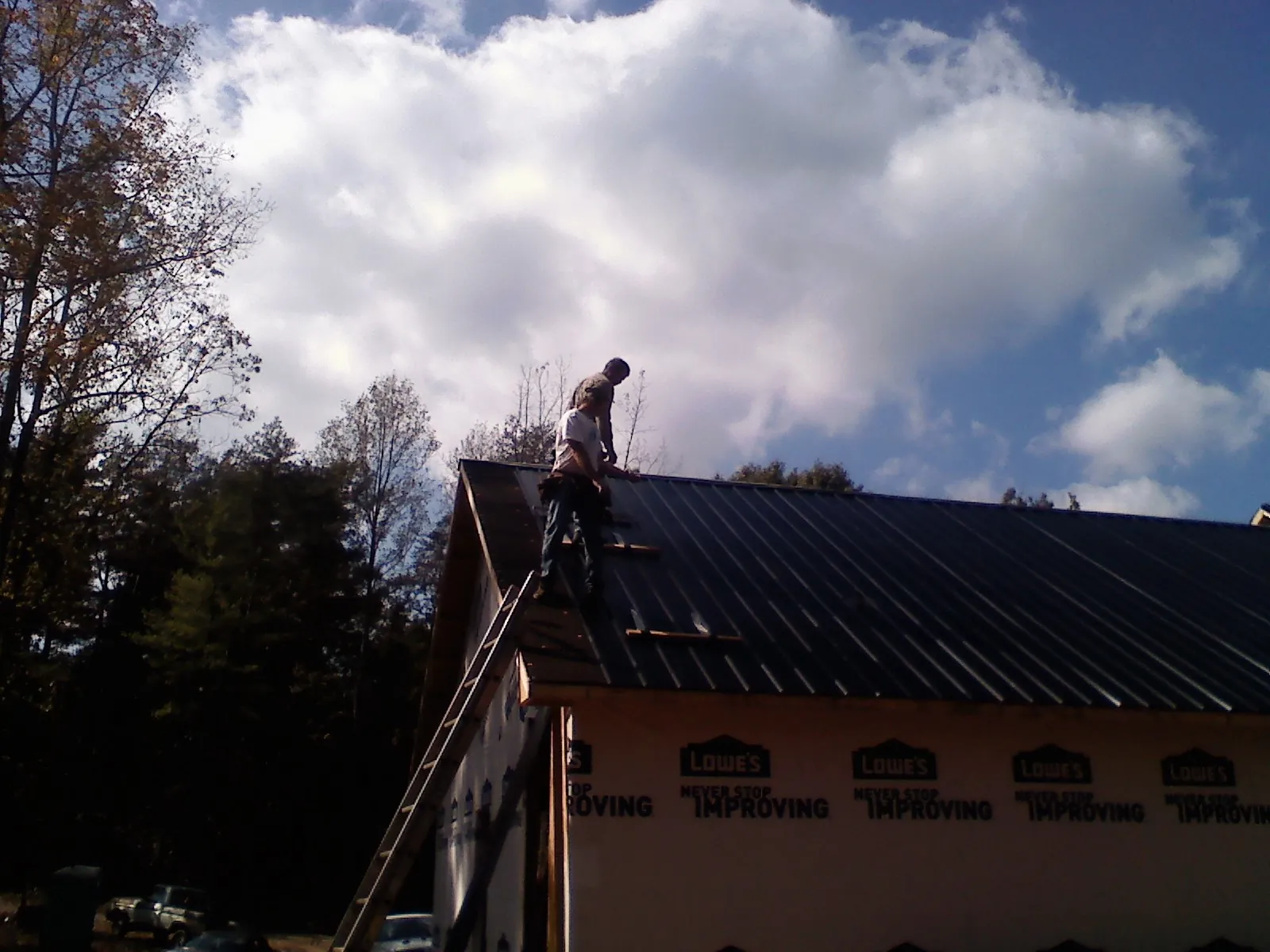 Roofer fastening dark metal panels high against a cloudy sky, from a Roof Inspection job in Tobias