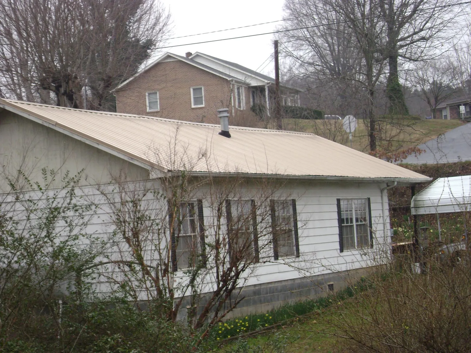 Tan metal roof on a white sided house set into a hillside — Commercial Roofing by Roofing Brothers in Tobias